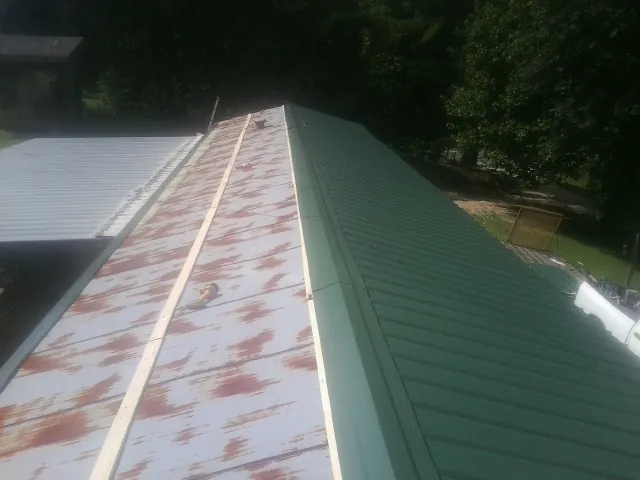Old rusted panels beside newly installed green metal roofing — Wind Damage Roof Repair by Roofing Brothers in Montezuma