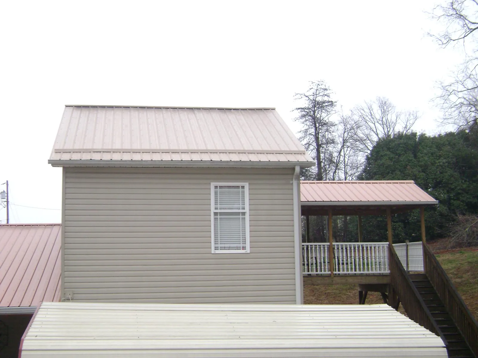 Tan metal roofs on a two story addition and attached porch, from a Roof Replacement job in Montezuma
